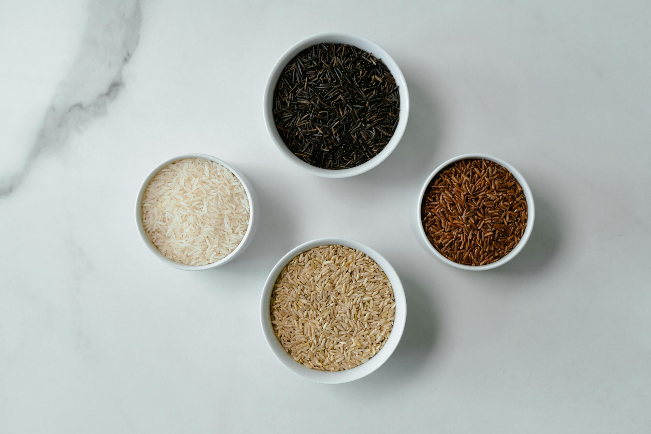 Four bowls showcasing different rice varieties on a marble surface, flatlay style.